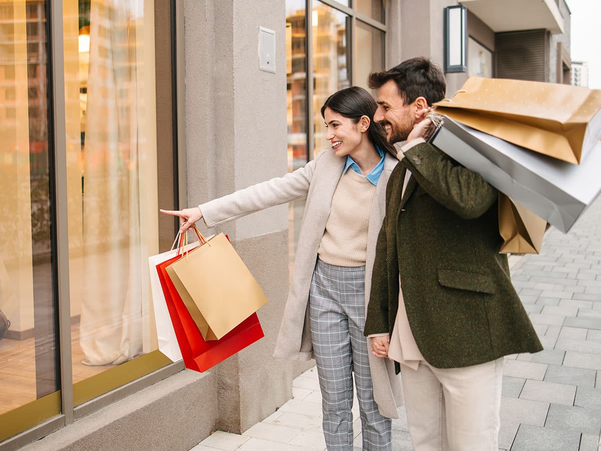 A man and woman stand outside a store, each holding shopping bags filled with purchases