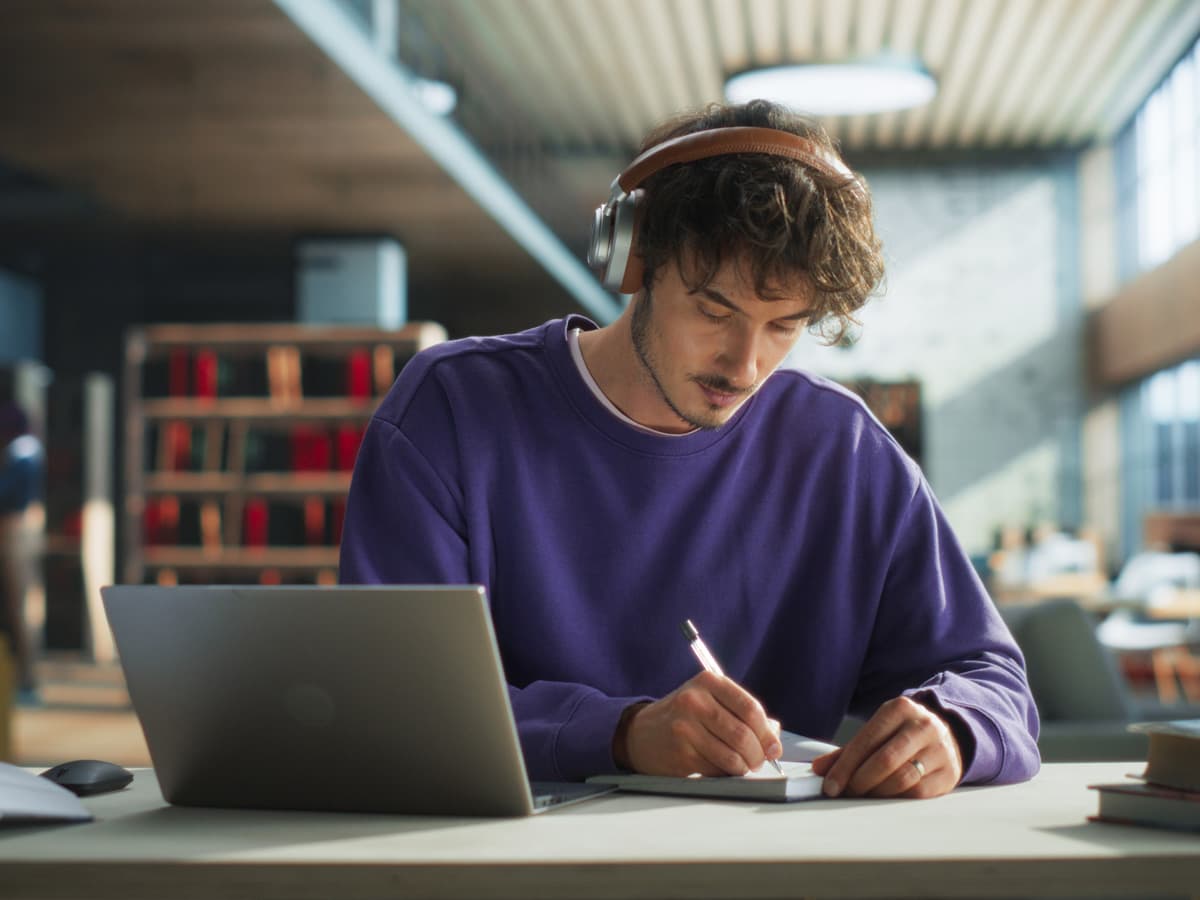 A man wearing headphones is focused on his laptop, engaged in work at a desk